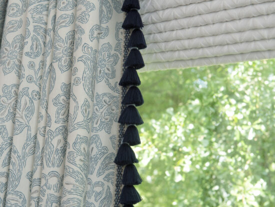 Custom drapery panels trimmed in fringe and hung over flat roman shade
